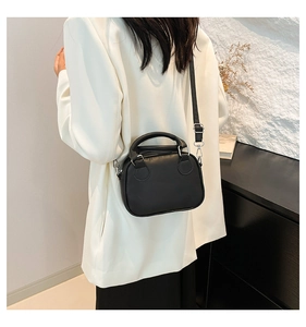 Mini black matte leather bowling bag with silver hardware on a white blazer model outfit
