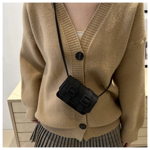 Detail of a black mini crossbody square bag with leather texture and double buckle design