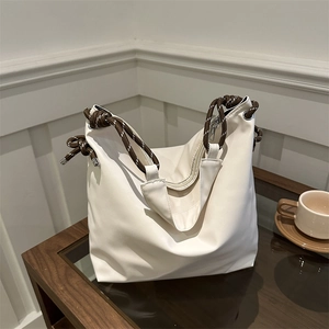Minimalist white faux leather tote bag with brown braided rope handle on a coffee table