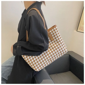 Detail of tweed tote bag showing brown check texture and leather handles with gold studs