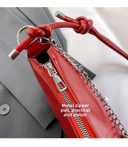 Detailed close-up of the silver zipper and metal chain on a red patent leather crescent bag