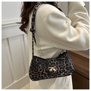 Close-up of leopard print baguette bag with golden bow clasp on white blazer model