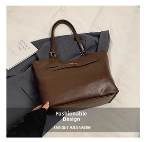 Close-up of brown textured leather tote bag with vintage gold buckle and slim strap