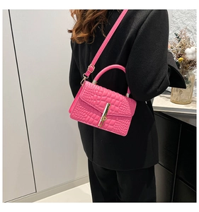 Detail of bright pink crocodile-textured handbag with gold clasp on black suit model