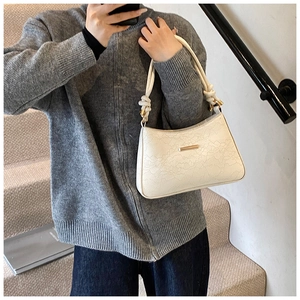 Detail of white baguette bag featuring lace-embossed texture and rope handle with gold hardware
