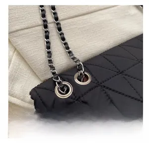 Detail of silver metal eyelet and leather-woven chain on black quilted shoulder bag