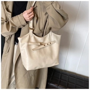 Detailed close-up of a large beige tote bag with gold buckle and smooth faux leather texture