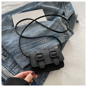 Close-up of black crocodile-embossed mini crossbody bag with double buckle flap details
