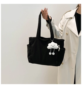 Detail of black corduroy tote bag featuring side pocket and cute cloud plush charm