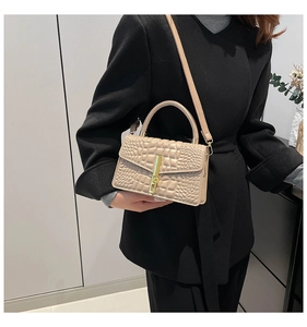 Detail of beige crocodile pattern handbag with gold clasp on black coat background