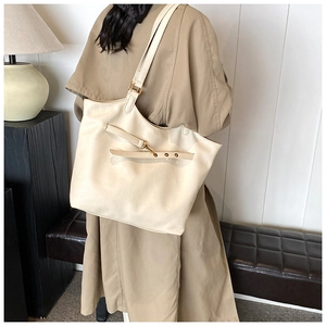 Detail of a creamy white large tote bag with decorative gold buckle on a model shoulder