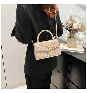 Detail of beige faux crocodile pattern handbag with gold clasp on a black blazer