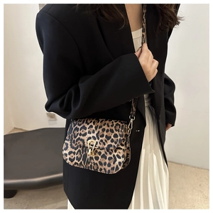 Model wearing leopard print crossbody bag with gold buckle over black blazer