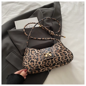 Detail of leopard print baguette bag with golden bow clasp on gray blazer