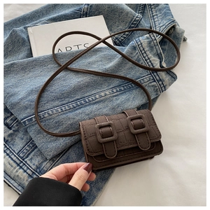 Detail of dark brown crocodile texture mini crossbody bag with double buckle flap on denim