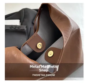 Detail of golden magnetic snap closure on brown pebbled leather tote bag for work