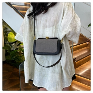 Détail du sac bandoulière bicolore élégant avec boucle dorée sur un mannequin en décor naturel