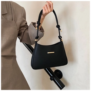 Detail of black underarm bag featuring knotted rope shoulder strap and gold hardware accents