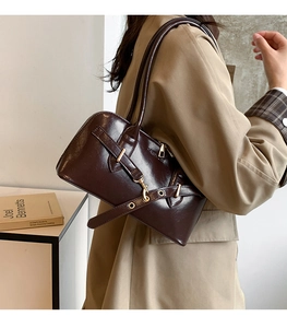 Detail of dark brown glossy leather handbag with buckle accent and zipper closure