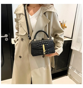 Detail of a black crocodile-textured handbag with gold hardware on a beige trench coat