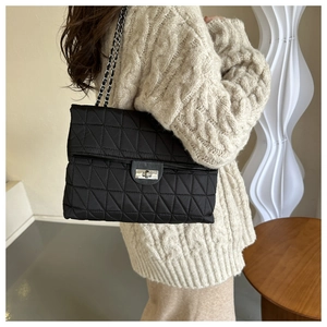 Detailed view of black quilted crossbody bag with metal chain strap worn by a model