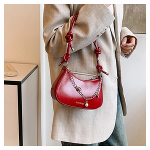 Detail of red glossy crescent bag with decorative chain and pearl charm detail
