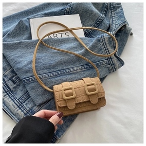 Detail view of khaki crocodile-embossed mini bag with double-buckle on denim and book