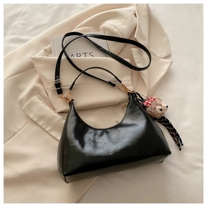 Detail of black oil wax leather hobo bag with teddy charm and silk scarf on white blazer