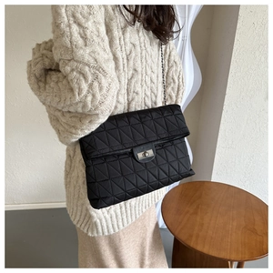 Detail of black quilted shoulder bag featuring triangle stitching and silver metal lock