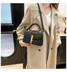 Detail of black crocodile embossed small square bag with gold vertical metal lock and handle