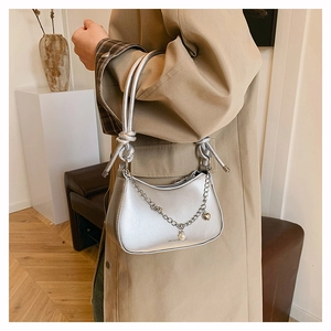 Detail view of silver crescent bag with metal chain, white pearl, and heart charm accents