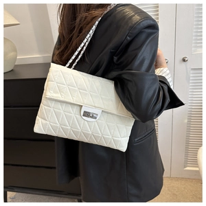 Detail of white quilted crossbody bag with silver chain strap shown on model's shoulder