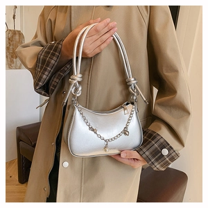 Detail of silver metallic underarm bag with knot handle, pearl pendant and chain