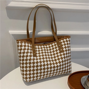 Brown woven tote bag with leather handles shown from a front angle on a white table