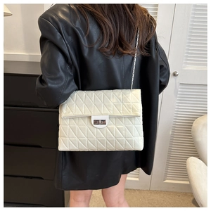 Detail of off-white quilted chain bag with silver lock worn over a black leather jacket