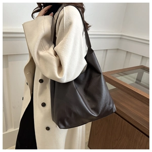 Detail of dark brown leather tote bag with wide strap on a model wearing a beige coat