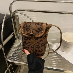 Sac bandoulière léopard en daim mat avec bordure en cuir posé sur une étagère chic