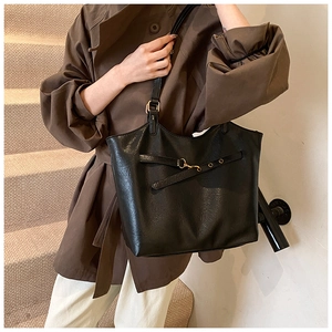 Detail of black matte tote bag with gold buckle strap worn by a model on stairs