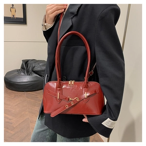 Close-up of red-brown glossy leather handbag with gold buckle and double handles on model
