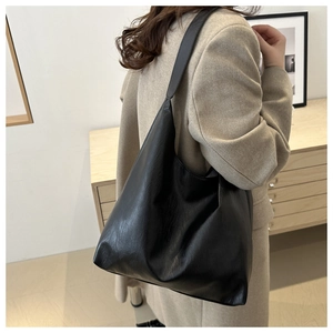 Detail view of large black glossy tote bag showing textured faux leather and modern hobo silhouette