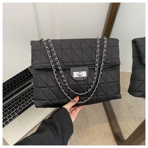 Close-up of black quilted tote bag with silver metal twist lock and chain strap detail