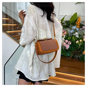 Sac bandoulière en cuir marron avec rabat tissé clair sur fond d'escalier en bois