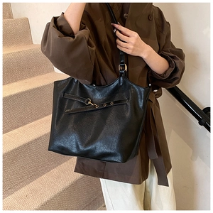 Detail view of a black leather tote bag with metal eyelets and decorative buckle strap