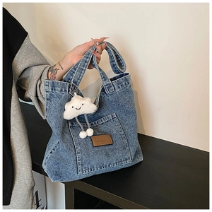 Détail du grand sac cabas en jean bleu avec écusson en cuir et breloque nuage en peluche