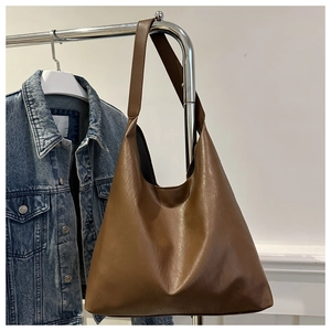 Close-up of a large dark brown matte leather tote bag hanging in a minimalist setting