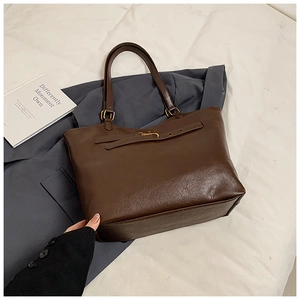 Macro shot of dark brown leather tote bag with grainy texture and golden buckle details