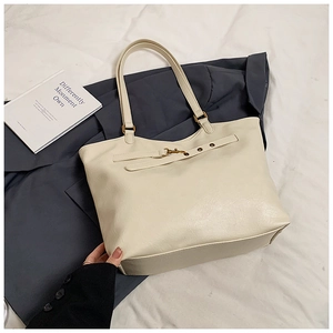 Detailed view of cream leather tote bag featuring vintage gold metal buckle and texture