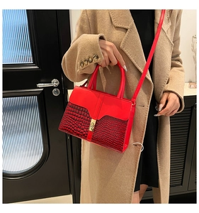 Detail of red faux crocodile leather handbag with golden clasp worn with a beige coat