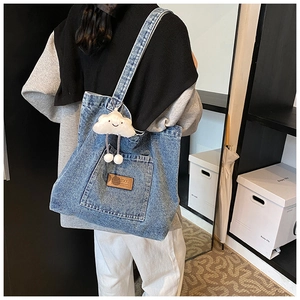 Détail du sac cabas en denim bleu avec petite poche avant et breloque en peluche nuage