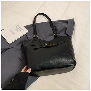 Detail of black faux leather tote with golden buckle and textured finish for office wear